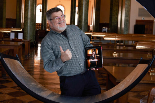 Ken Huth with big smile and giving thumbs up holding an iPad with a portrait on it